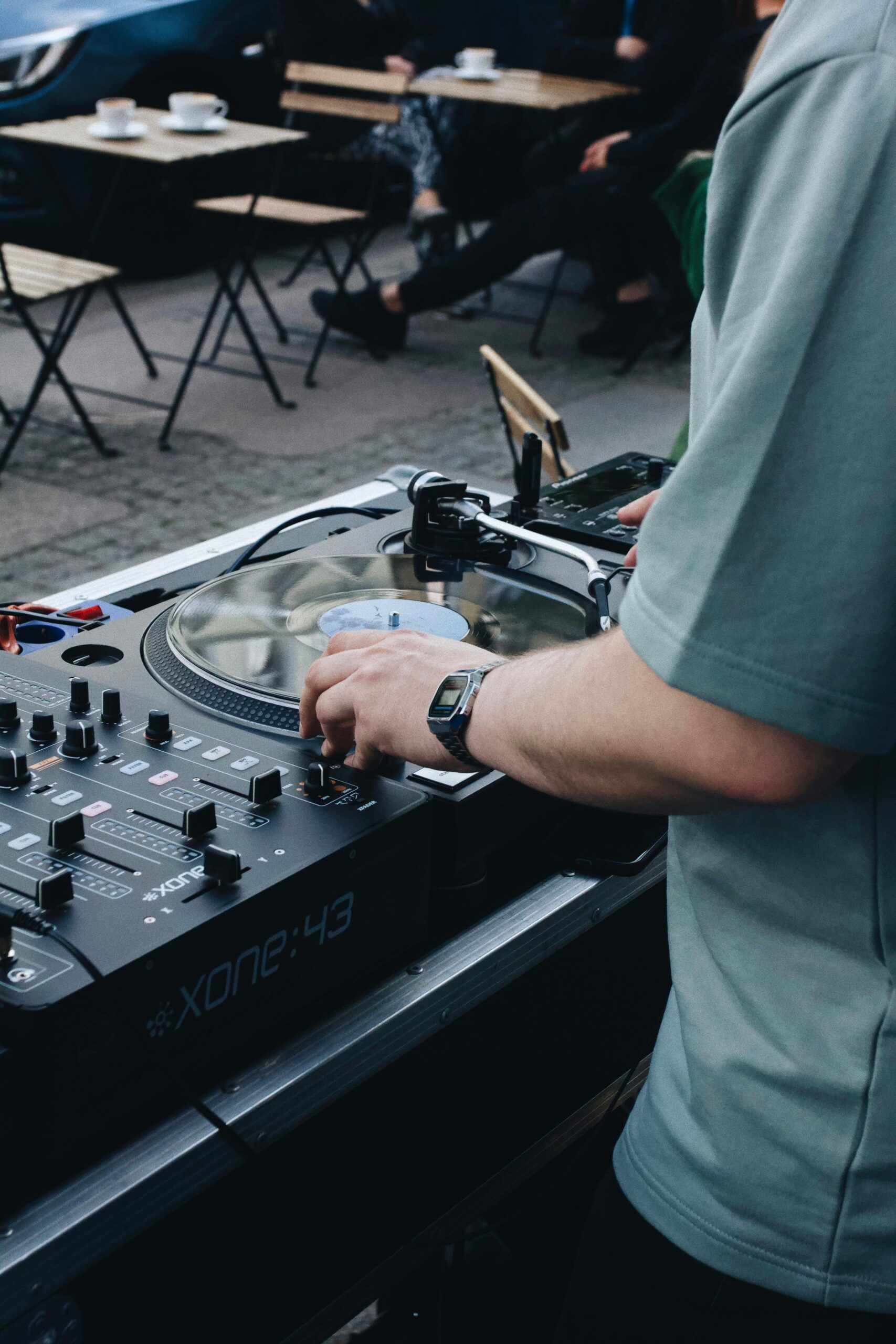 DJ adjusting audio mixer at an outdoor café in Szczecin, Poland, creating vibrant tunes.